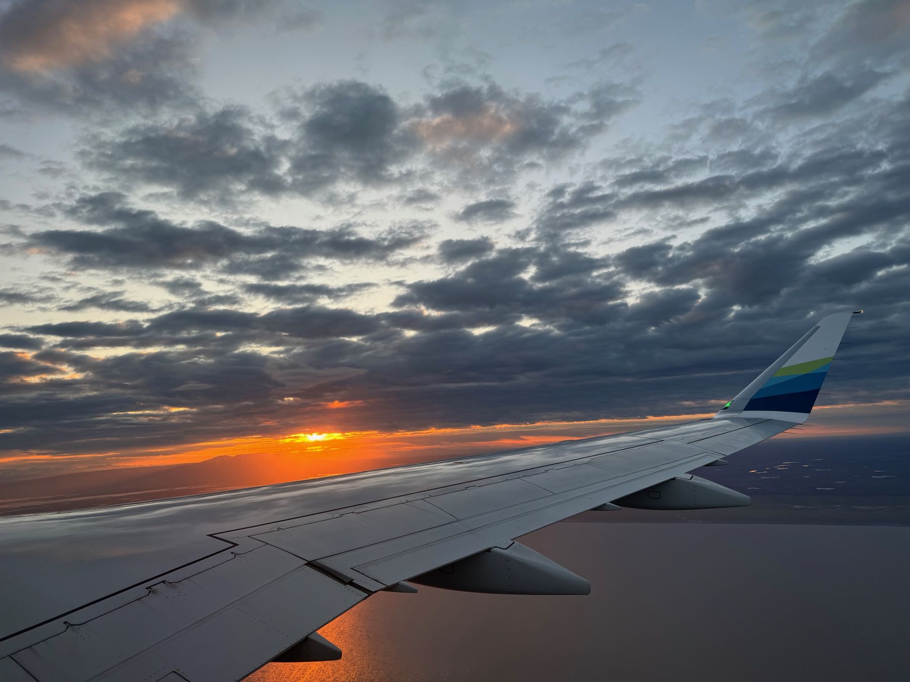 Sunset over clouds seen past an airplane wing