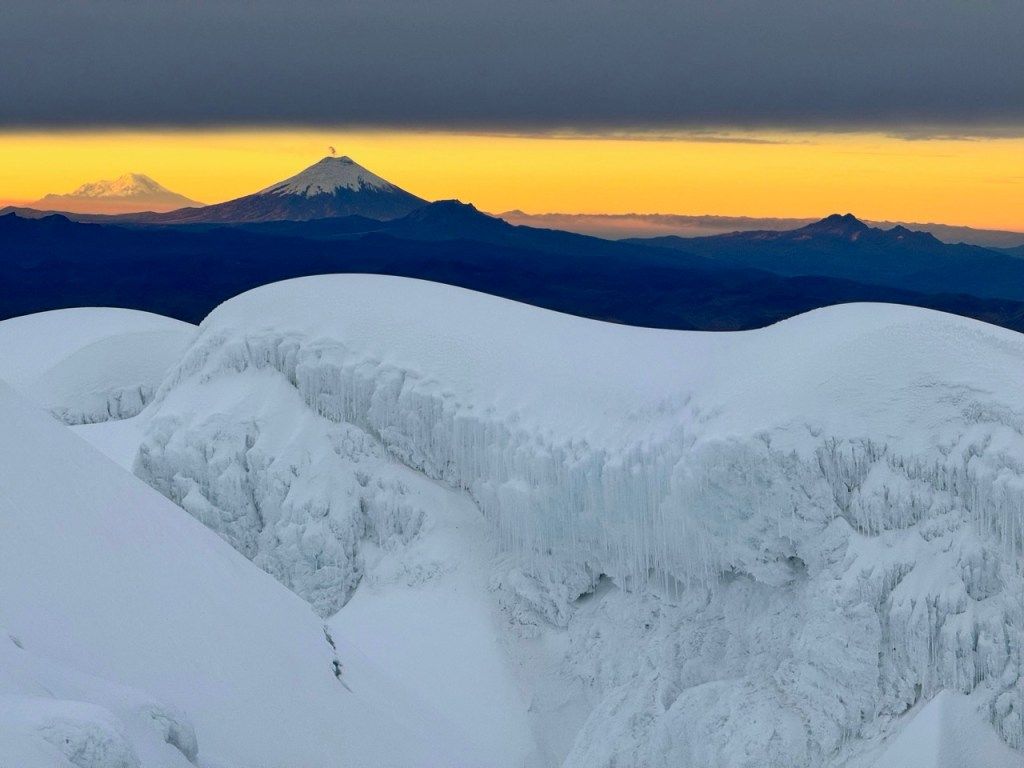 A distant peak above the clouds at sunrise, seen across snow